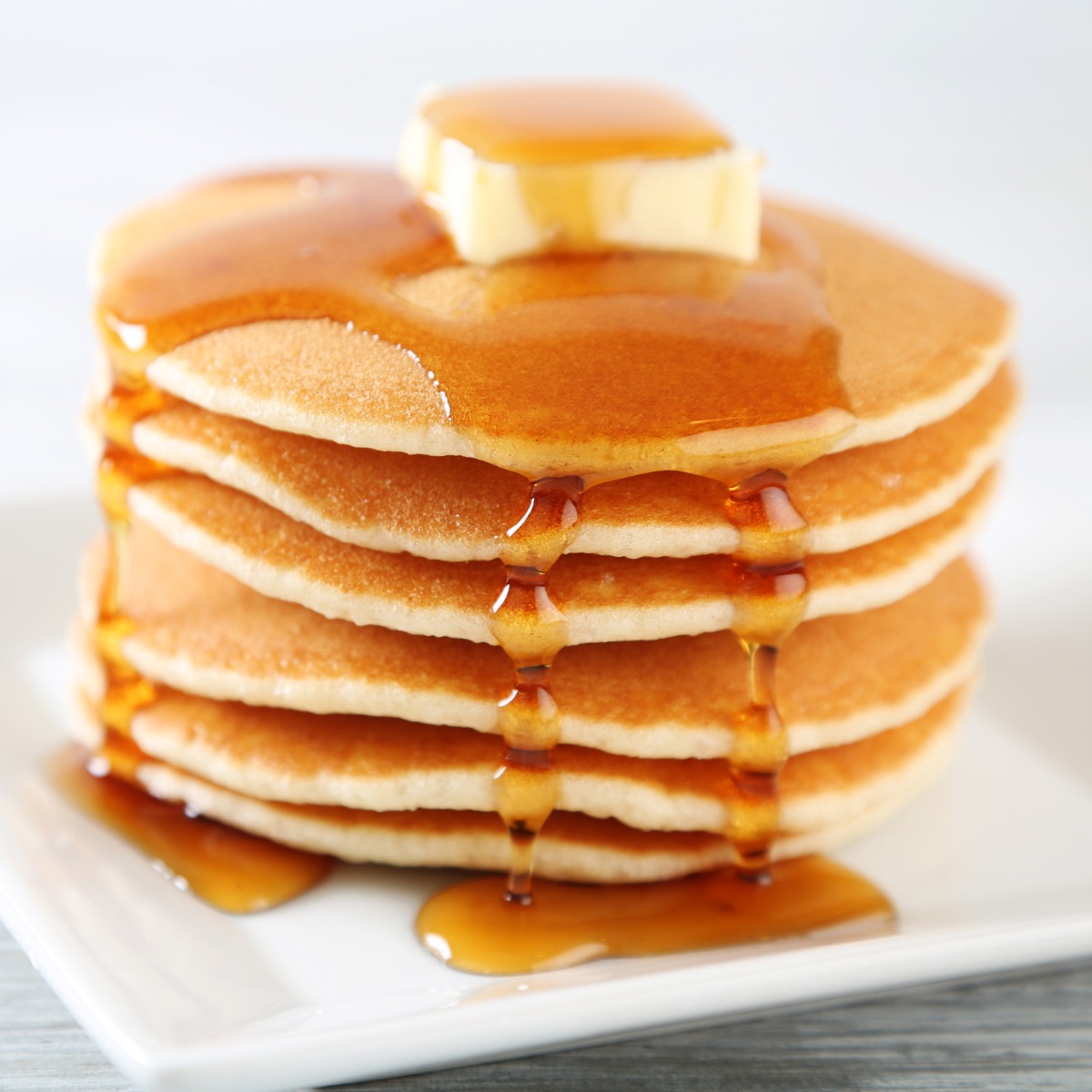 Amerykańskie Pancakes ułożone na talerzu, podane z syropem klonowym i kostką masła.