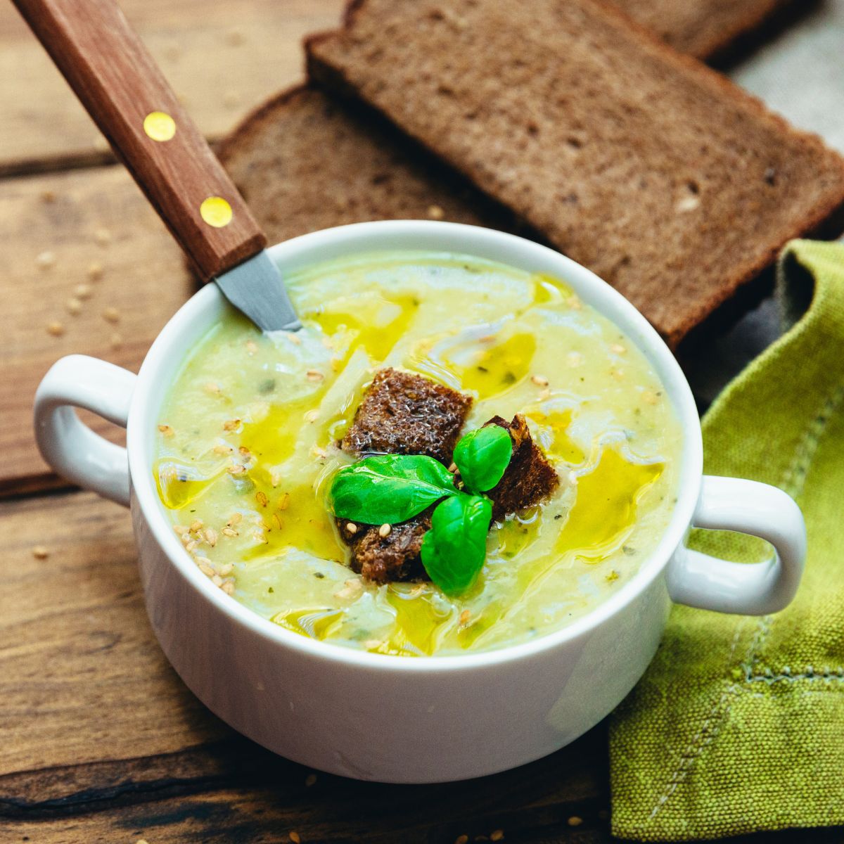 Zupa krem z cukinii podana w misce z grzankami, oliwą z oliwek, prażonym sezamem i świeżą bazylią.