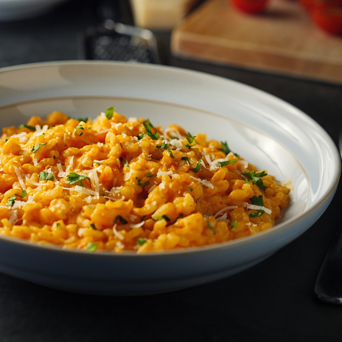 Risotto pomidorowe podane w głębokim naczyniu z dodatkiem parmezanu i świeżych ziół.