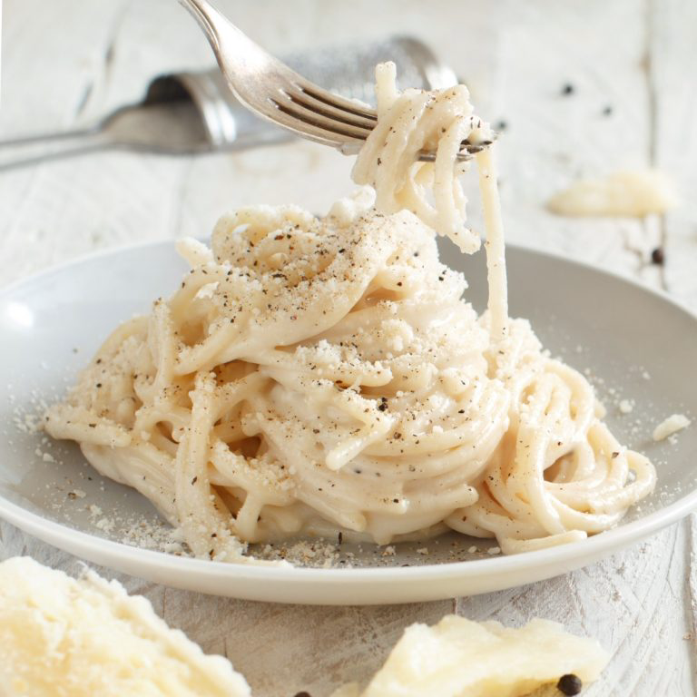 Bezglutenowy makaron z serem Podany na talerzu z dodatkową ilością pecorino i czarnego pieprzu na wierzchu.