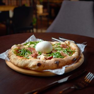 Pizza z burratą, rukolą i prosciutto, podana na talerzu.