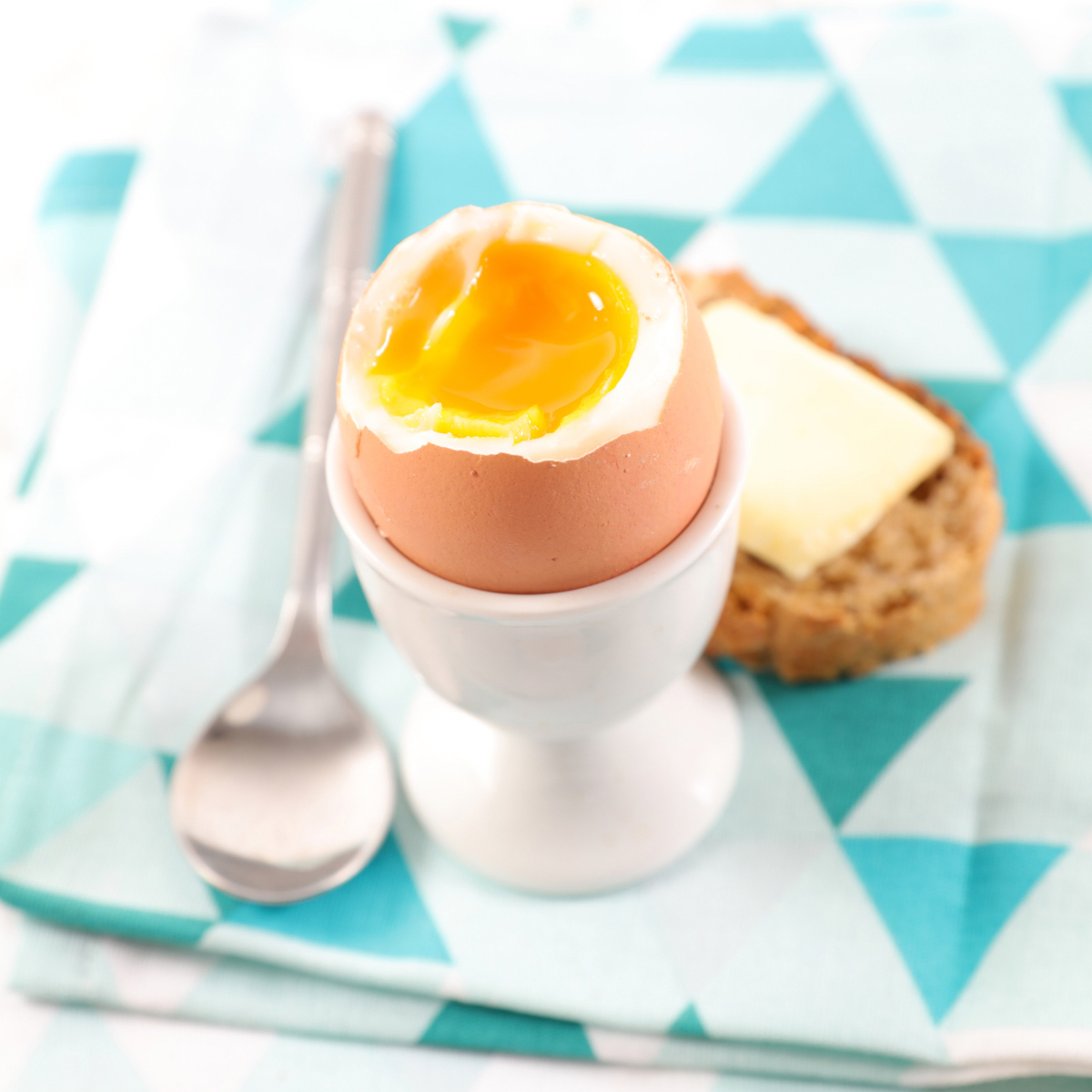 Jajko na miękko, podane na podstawce do jajka z dodatkiem pieczywa i masła.